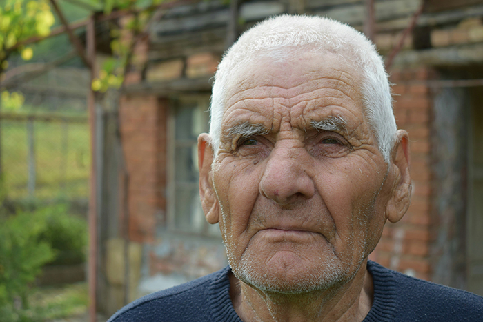 Elderly man with a solemn expression outdoors, reflecting on disturbing deathbed confessions and lifelong guilt.