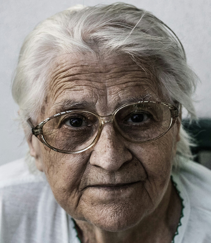Elderly woman with glasses, looking solemn, representing disturbing deathbed confessions and deep guilt.