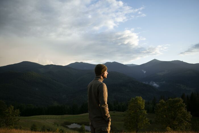 Man standing in a mountainous landscape at sunset, reflecting raw and emotional confessions carrying heavy secrets.