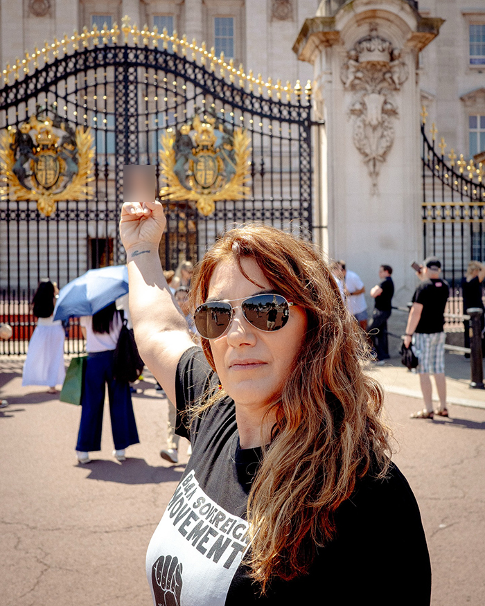 Aboriginal artist wearing sunglasses and raising a fist in front of Buckingham Palace gates during a protest. Aboriginal artist wearing sunglasses and raising a fist in front of Buckingham Palace gates during a protest.
