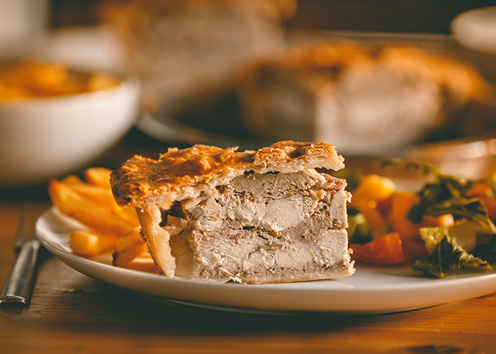 Slice of classic chicken pot pie with a golden crust served with fries and vegetables at a family gathering.