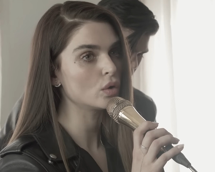 Sharon Osbourne's rarely-seen daughter speaking into a microphone with a focused expression indoors.