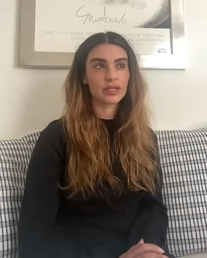 Sharon Osbourne's rarely-seen daughter sitting on a couch with long hair and a black top in a casual setting.