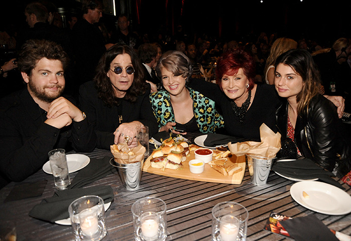 Sharon Osbourne&rsquo;s daughter with Ozempic rumors, smiling at a table with family, sandwiches and drinks in a dimly lit setting.