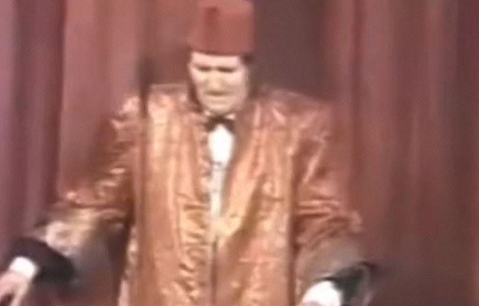 Man in a shiny patterned suit and fez hat performing on stage during a shocking moment on live television for Gen X viewers.