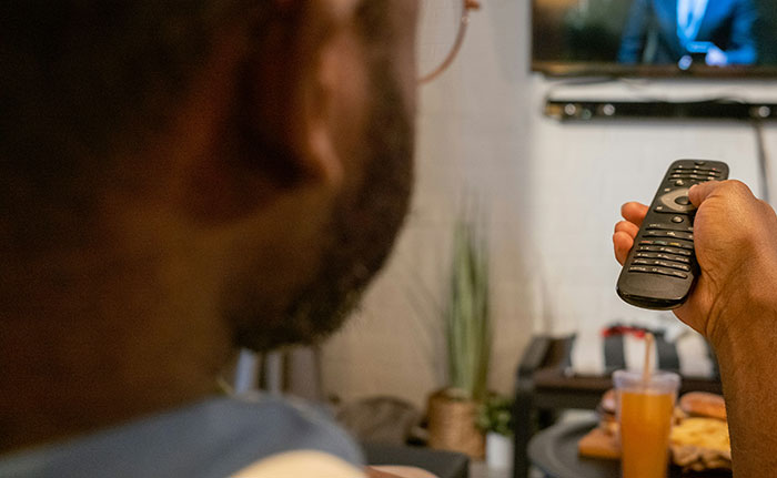 Person holding a remote control watching live television showing a shocking moment in a home living room setting.