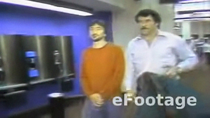 Two men in casual clothes standing inside a room, part of shocking moments on live television footage.