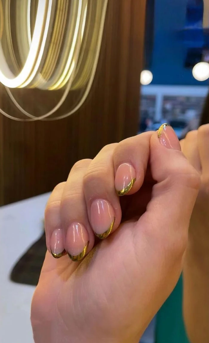 Short French tip nails with gold design on a hand, showcasing stylish nail art trends for 2025. Short French tip nails with gold design on a hand, showcasing stylish nail art trends for 2025.