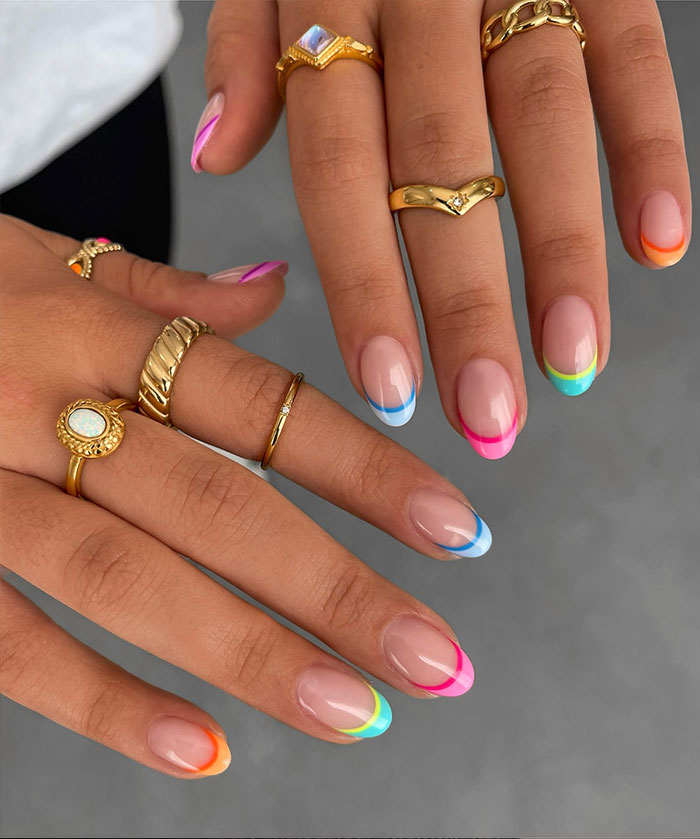 Short French tip nails with colorful design on natural nails, styled with gold rings on fingers. Short French tip nails with colorful design on natural nails, styled with gold rings on fingers.