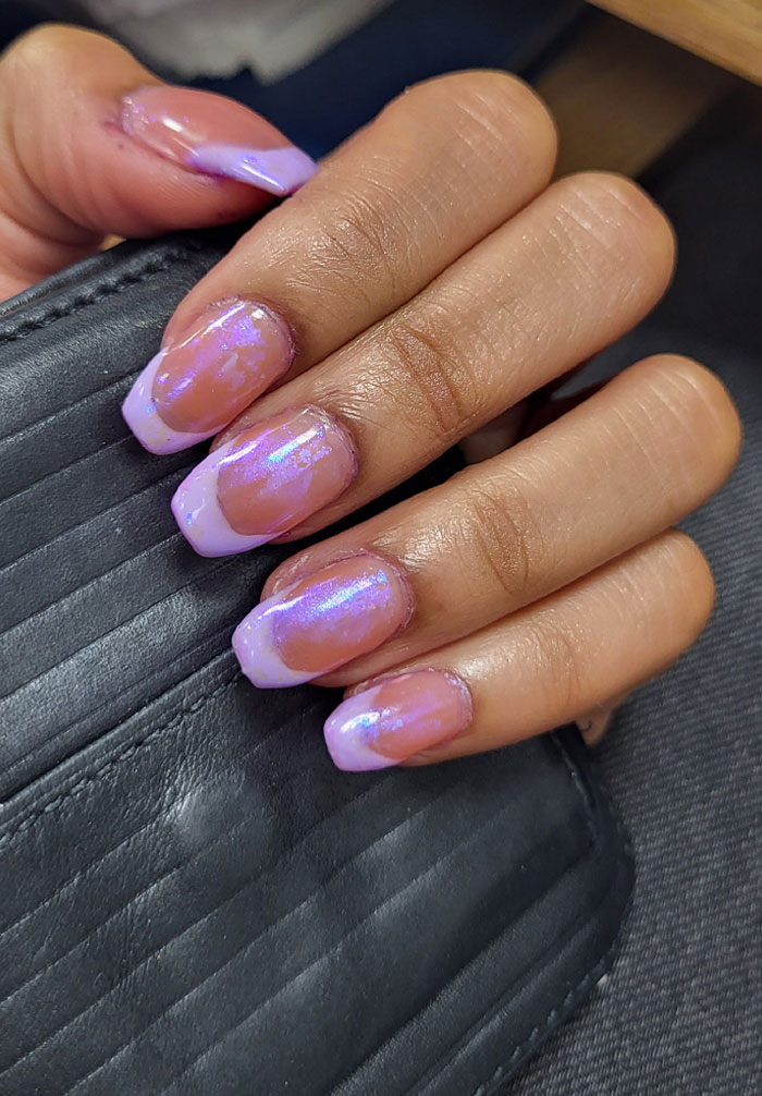 Hand with short French tip nails featuring iridescent purple designs on a black textured surface. Hand with short French tip nails featuring iridescent purple designs on a black textured surface.