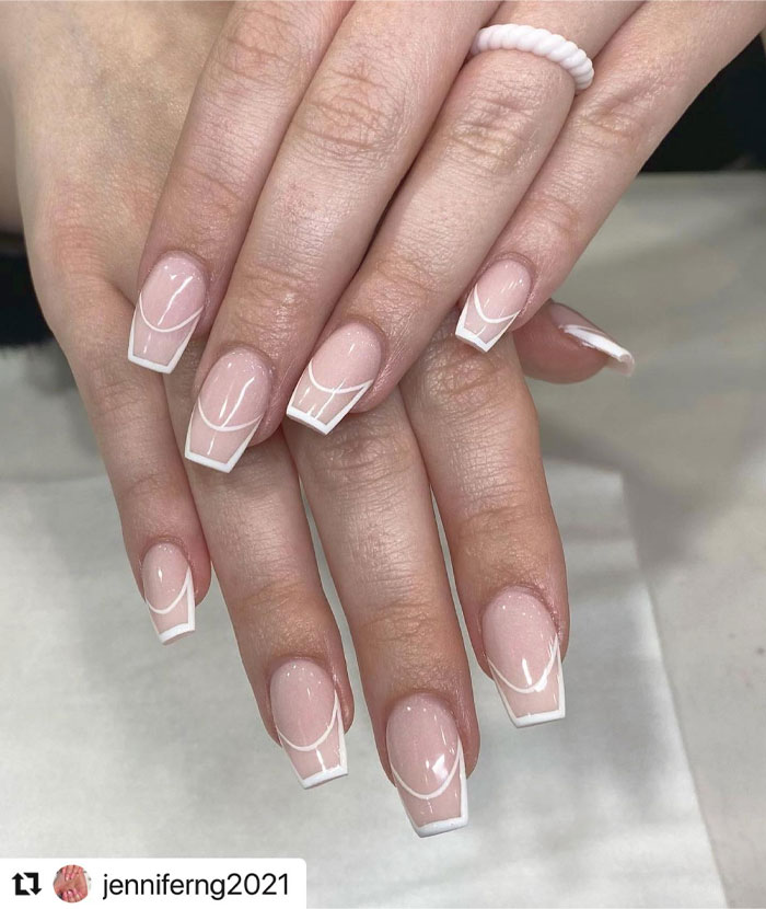 Short French tip nails with modern white line designs on nude base, showcasing stylish and trendy nail art for 2025.
