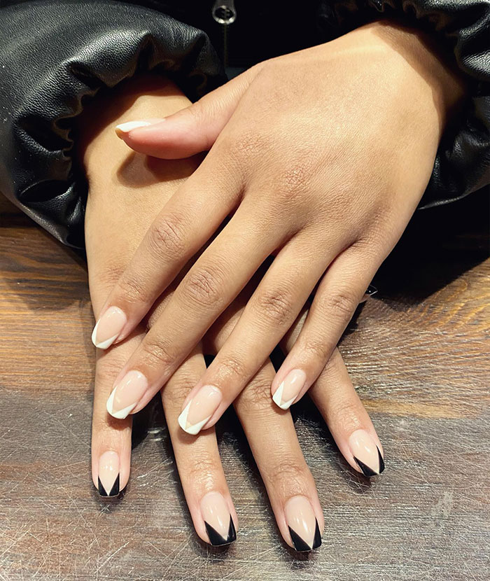 Hands with short French tip nails featuring chic black and white design on a wooden surface, showcasing stylish nail art trends. Hands with short French tip nails featuring chic black and white design on a wooden surface, showcasing stylish nail art trends.