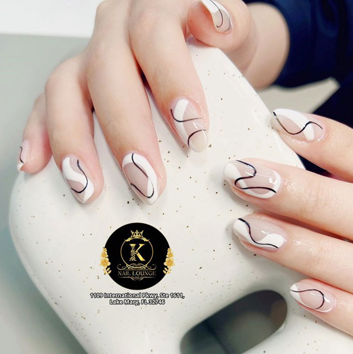 Short French tip nails with stylish black swirl design on neatly manicured hands holding a white speckled object.
