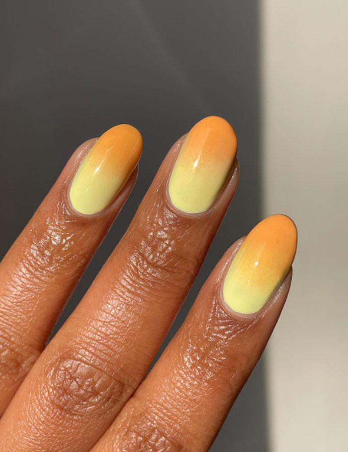 Short French tip nails with yellow and orange gradient design on well-groomed fingers showcasing style trends.