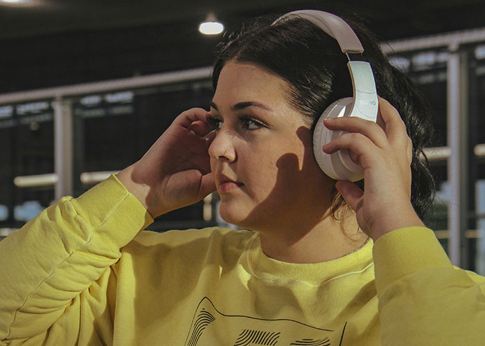Woman at the gym wearing headphones and a yellow sweatshirt focusing on workout, embodying gym mindset and determination.
