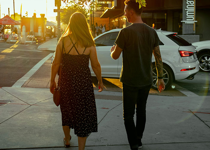 Woman and gym guy walking on sidewalk at sunset, gym guy reaching out for a fist bump despite her disinterest.