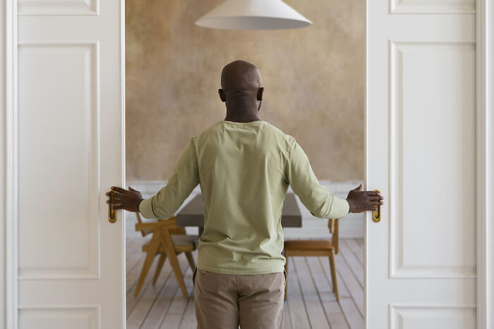 Man opening double doors to an empty room, symbolizing hesitation and challenges of being shy in social situations.