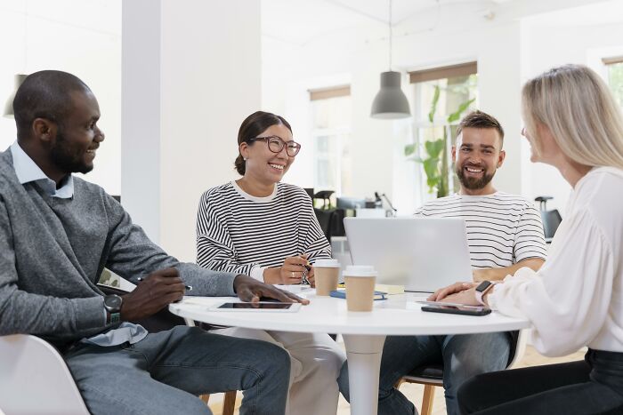 A diverse group of coworkers smiling and discussing ideas around a table in a bright office setting about being shy.
