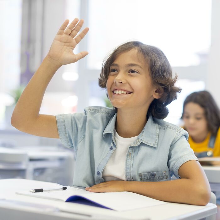 Smiling shy boy raising hand in classroom, experiencing moments that made being shy 10x worse for some students.