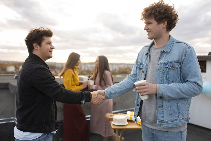 Two young men awkwardly shaking hands outdoors, illustrating challenges of being shy in social situations.