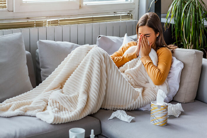 Woman lying on couch covered with blanket, appearing sick and using tissues, reflecting things people thought everyone knew.