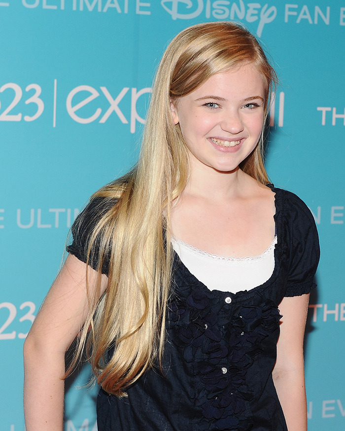 Young female child star with long blonde hair smiling at a Disney fan event, showcasing an unrecognizable transformation.
