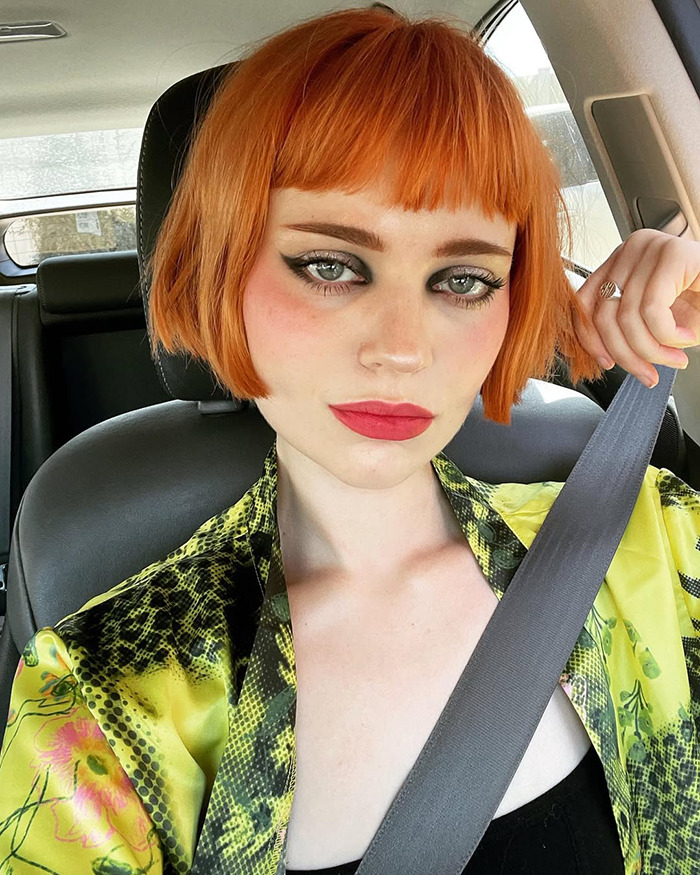 Young woman with orange bob haircut and bold makeup, wearing a patterned outfit, showcasing a child star's unrecognizable transformation.