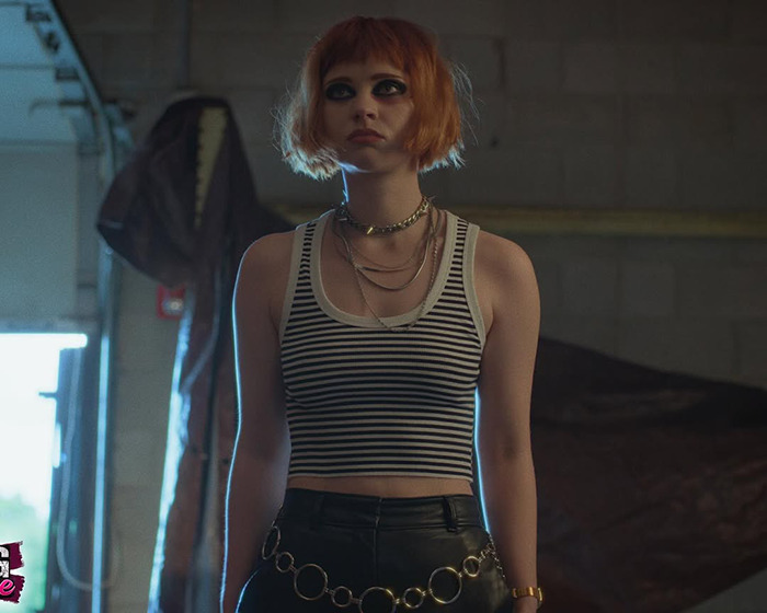 Young woman with orange hair and dark eye makeup wears striped tank top and leather pants, highlighting child star transformation.