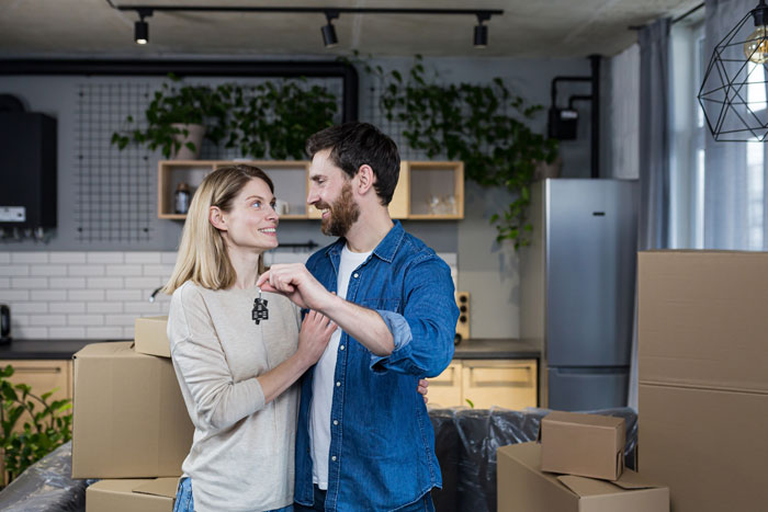 Couple happily holding house keys surrounded by boxes, symbolizing a new house and family moving in together. Couple happily holding house keys surrounded by boxes, symbolizing a new house and family moving in together.