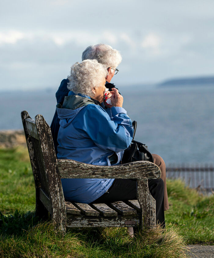 Two elderly people sitting on a weathered bench by the sea, emphasizing tobacco habits and health awareness.