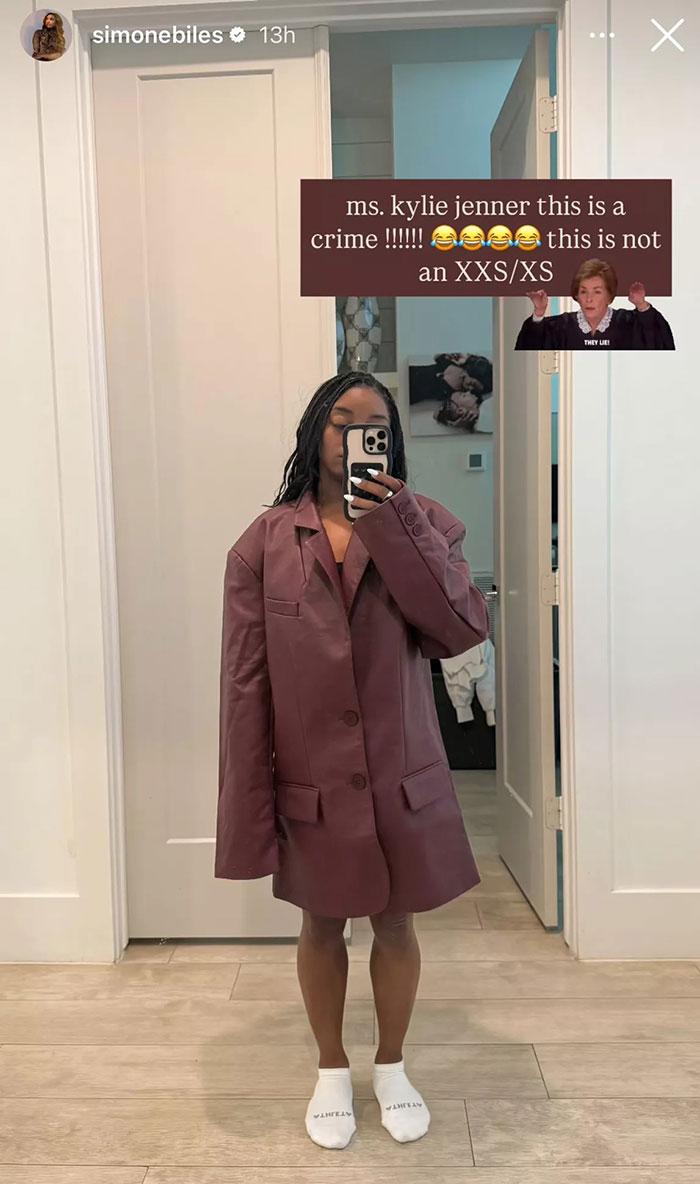 Simone Biles taking a mirror selfie wearing an oversized jacket from Kylie Jenner's clothing line, criticizing the fit.