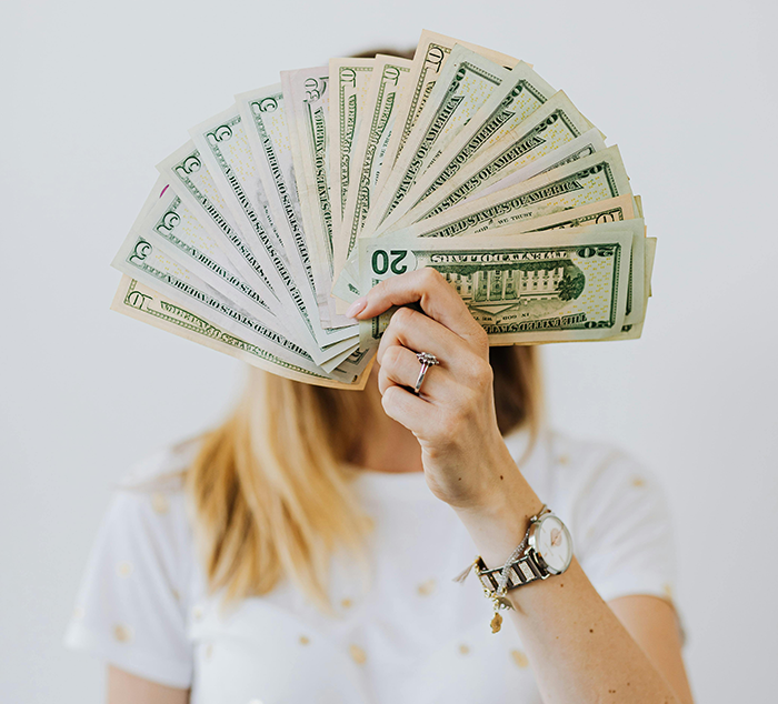 Woman holding a fan of cash representing drama after bride spends $25K savings and expects sister to fund wedding expenses