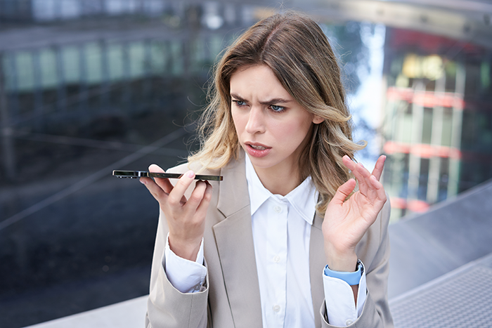 Frustrated woman in business attire speaking on phone outside, reflecting drama after bride splurges savings and expects sister to fund wedding