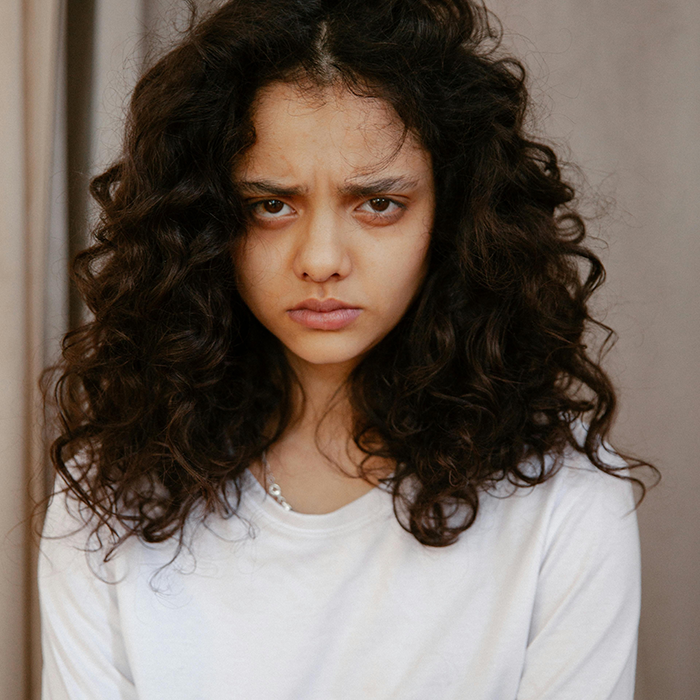 Young woman with curly hair and serious expression, representing sister force and sibling babysit challenges.