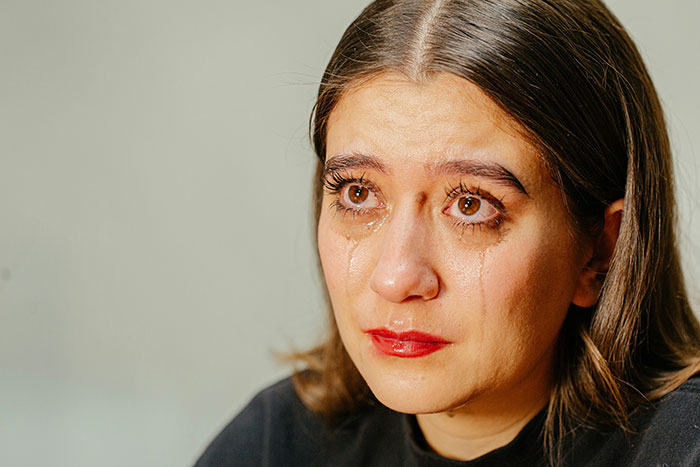 Woman with tears streaming down her face, showing sadness on graduation day after seat given away without word.