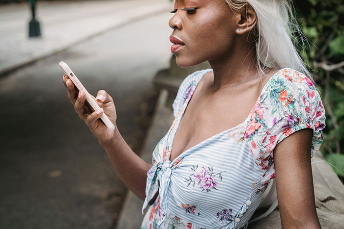 Woman with long blonde hair looking at phone outdoors, reflecting on graduation day ruined by hubby seating issue.