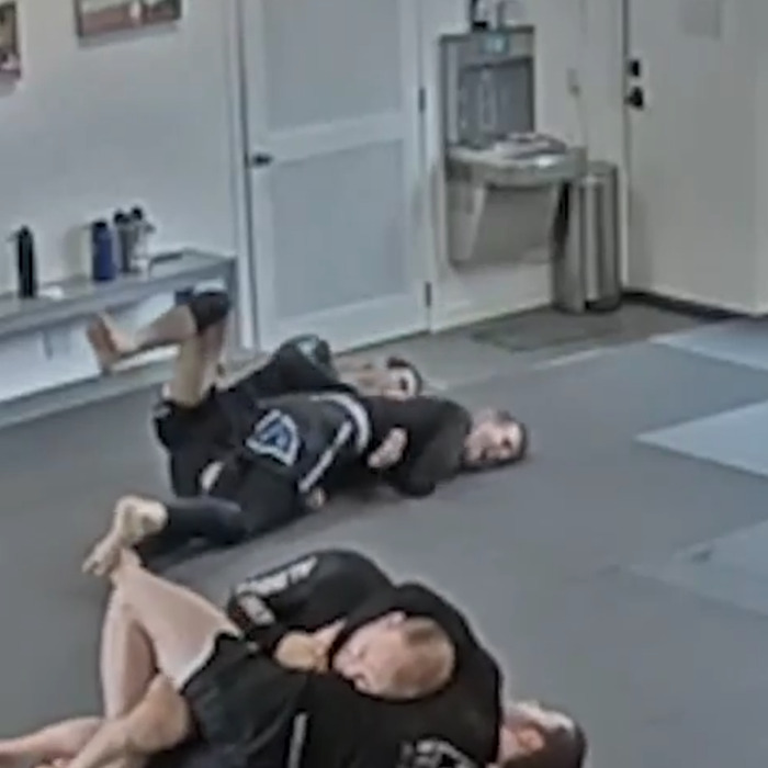 Two men in black gis practicing Brazilian Jiu-Jitsu grappling on mats in a gym during a tragic freak accident sparring incident.