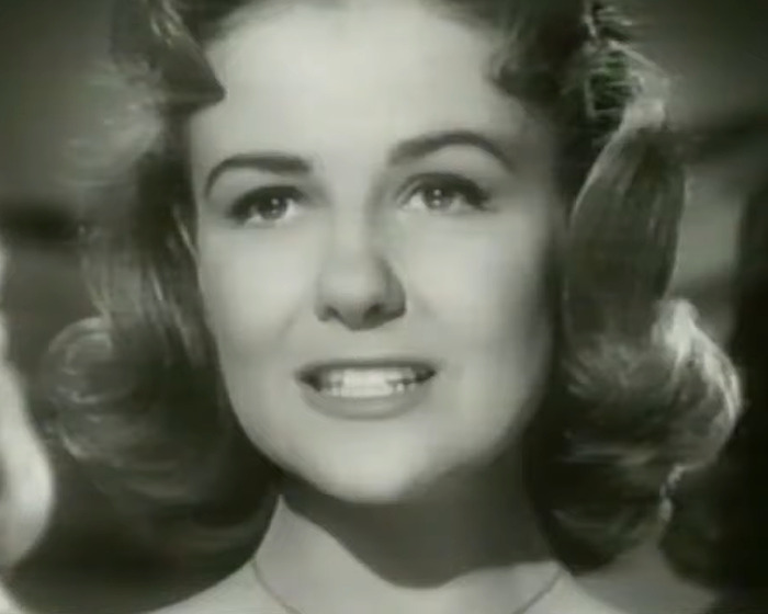 Black and white close-up of iconic sitcom legend smiling with curled hair, reflecting on a memorable moment.