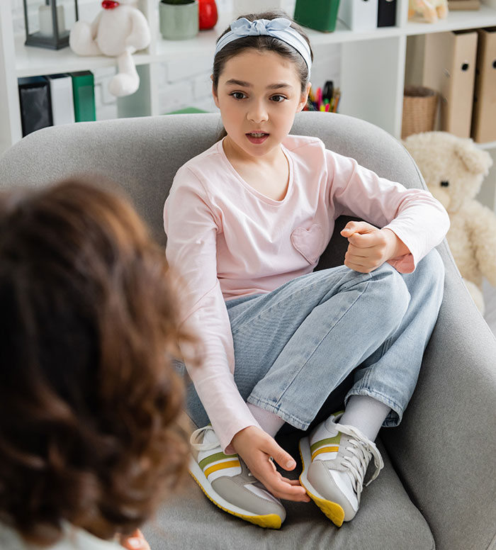 Young girl sitting in a chair talking to an adult, illustrating kids lies that started off silly and got real.