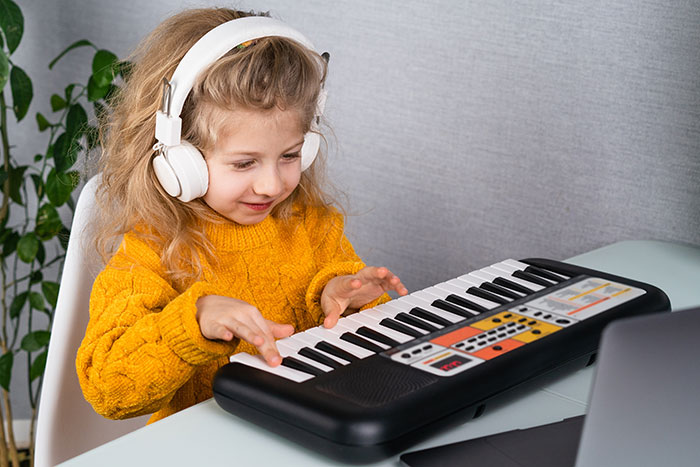 Young girl in yellow sweater wearing headphones playing keyboard, illustrating common kids lies that started silly and got real.