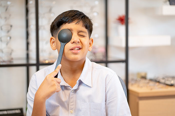 Young boy in white shirt playfully holding a spoon over his eye illustrating kids lies that started off silly.