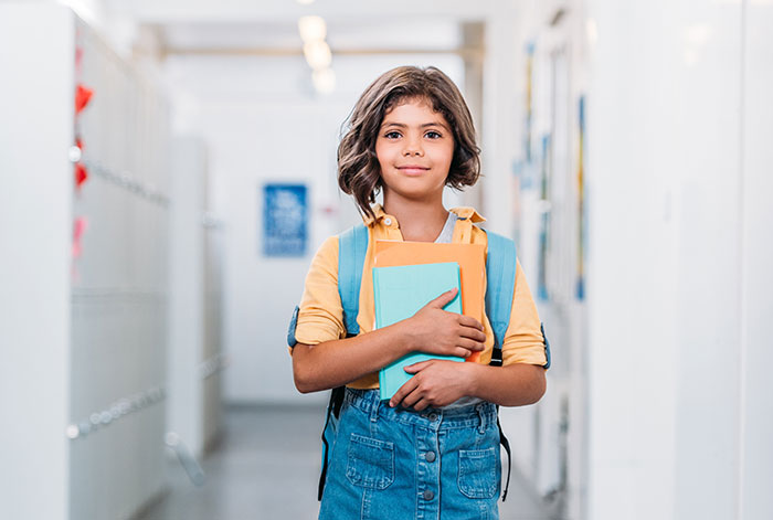 Young girl in a school hallway holding books, representing kids' lies that started off silly and got way too real.