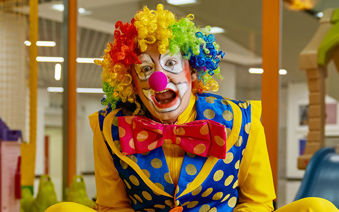 Clown with colorful wig and makeup making a funny face, illustrating kids' lies that started off silly and got real.