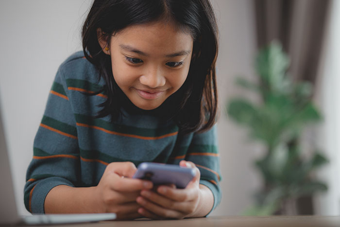 Young girl smiling while looking at a smartphone, illustrating kids' lies that started off silly and got real.