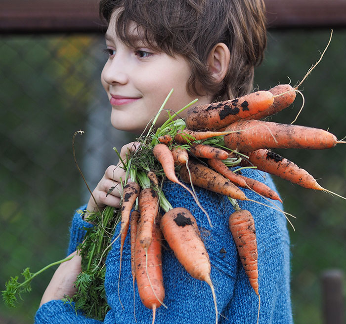 Child holding freshly picked dirty carrots from garden, illustrating kids lies that started off silly and got real moments.