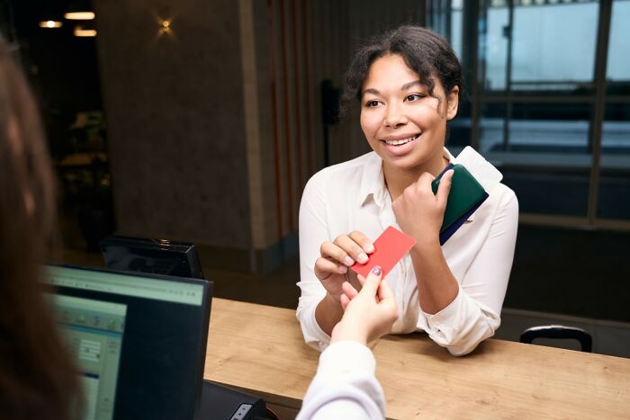 Woman smiling at a service desk, holding travel documents and credit card, demonstrating easy golden travel hacks.