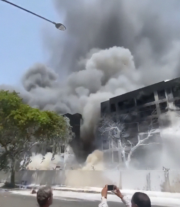 Smoke billowing from a damaged building as people capture the scene, related to Air India tragedy and stars apologizing.