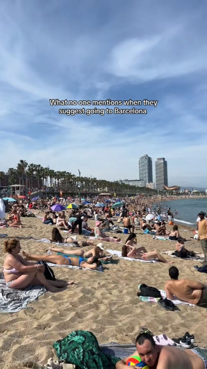 Crowded beach in Barcelona with many travelers under umbrellas, showing Instagram vs reality travel moments in popular destinations.