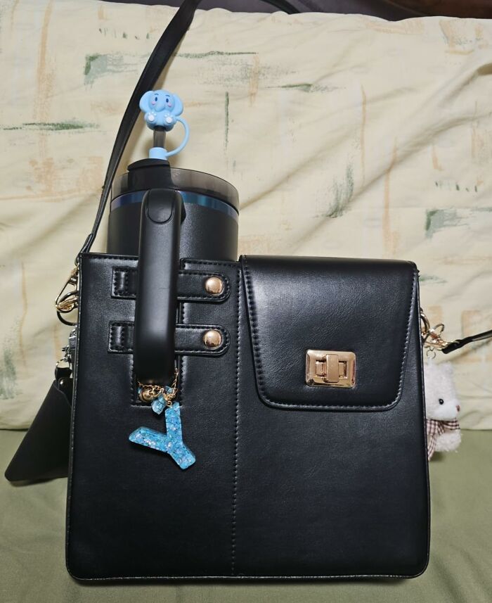 Black leather handbag with gold clasp, blue water bottle featuring an elephant cap, and a sparkly blue keychain charm.
