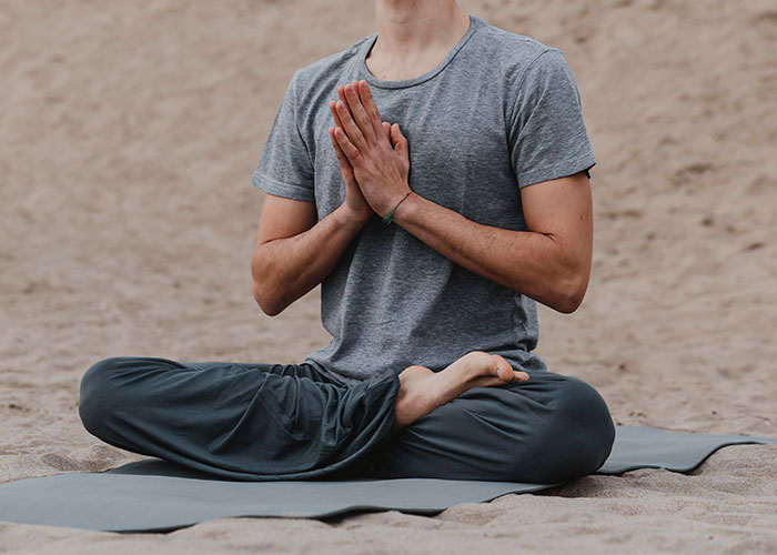 Person sitting cross-legged on a mat meditating with hands in prayer position, symbolizing life story change and new beginnings.